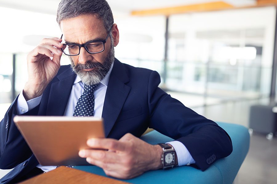 Blog - Businessman Sitting In Modern Office Looking At His Tablet