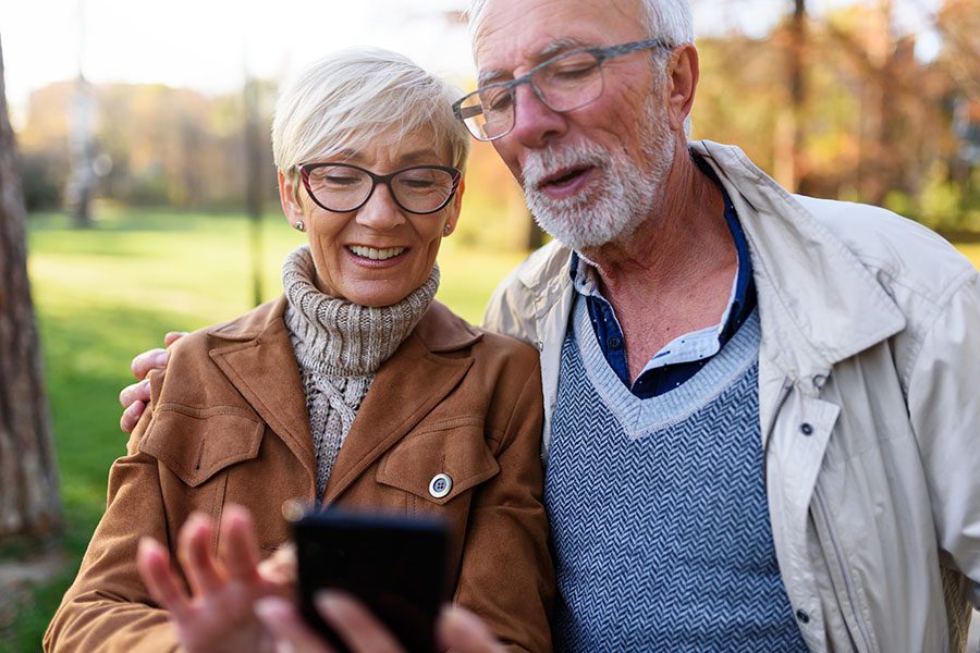 Older Couple Standing Outside In Park Using Their Phone